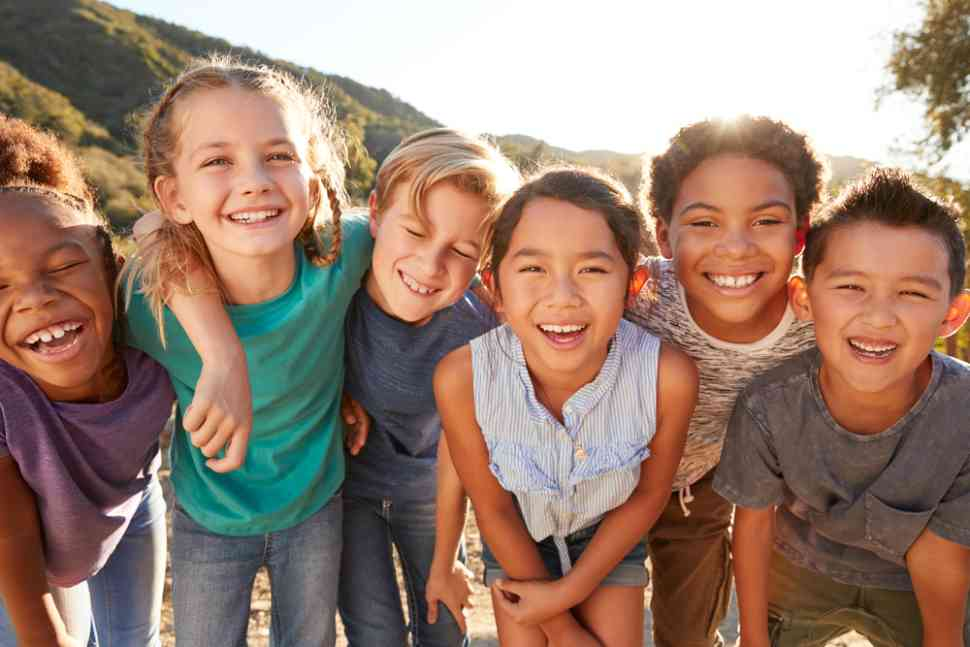 A group of smiling children laughing together outdoors in warm sunlight