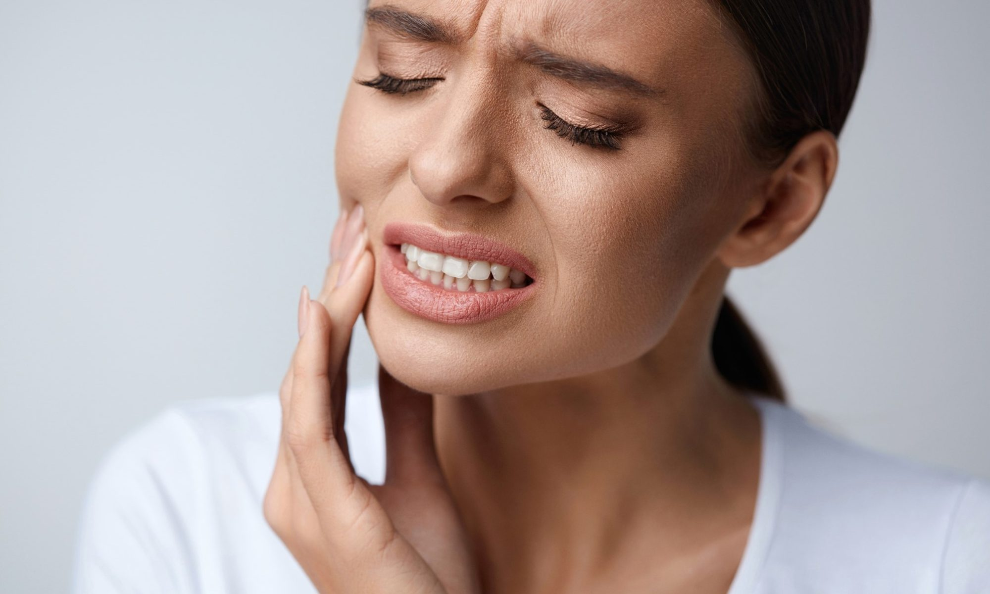 Woman holding her jaw in discomfort against a soft neutral background