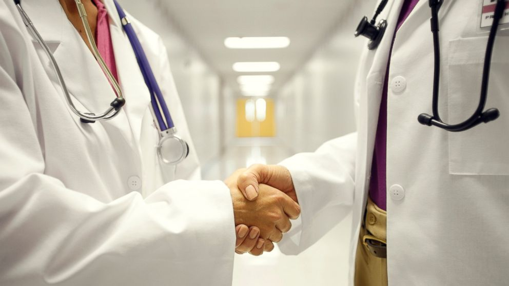 Two clinicians in white coats shaking hands in a clinic hallway
