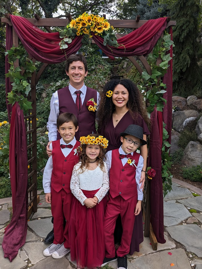 Dr. Brittany Johansen and Dr. Ryan Hart with their family outdoors under a sunflower arbor